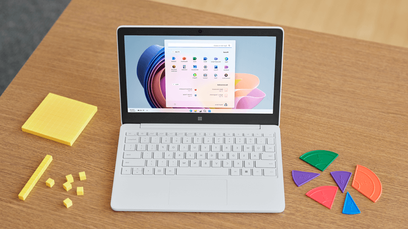 Surface Laptop SE مفتوح داخل Glacier على مكتب مدرسة مع شاشة Windows 11 SE ظاهرة.