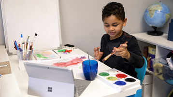 يستخدم طفل صغير الرسامات على الورق بينما يشاهد كمبيوتر Surface محمولا ومفتوحا 