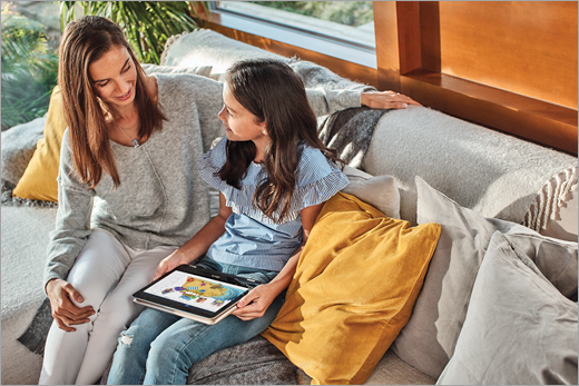 Майка и дъщеря й седят на дивана, докато дъщерята използва Paint 3D на лаптоп