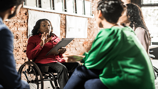 Бизнес дама в инвалидна количка, водеща групова дискусия в творчески офис