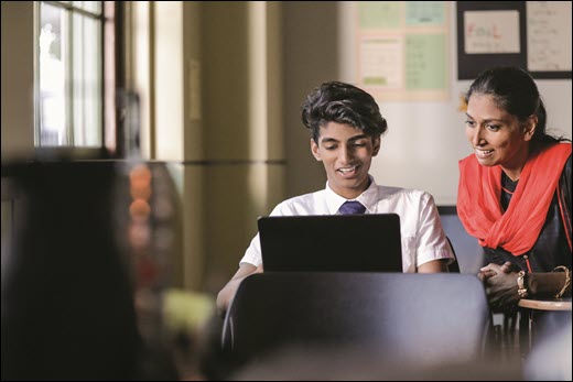 Снимка на учител и ученик, който гледа компютър.