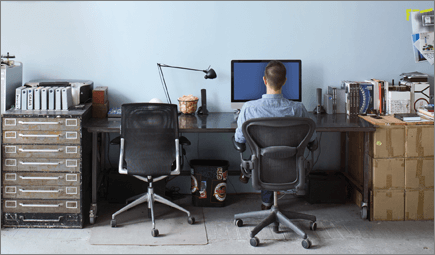 Снимка на човек, който седи на бюро и работи на компютър.