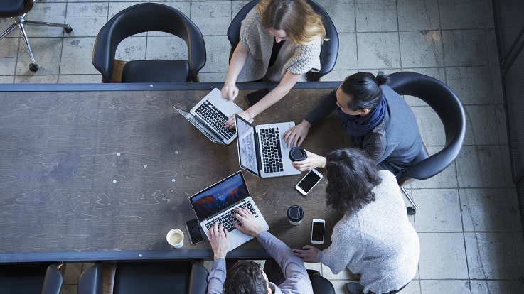 снимка над четирима души, работещи на компютри и устройства на маса