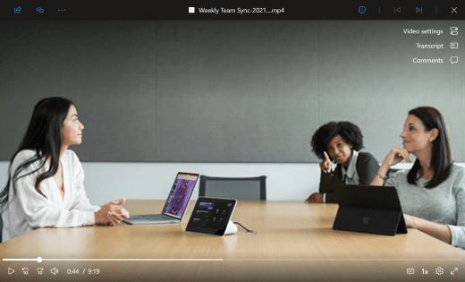 Přehrávač videa zobrazuje probíhající schůzku v Teams. Tři pracovníci kanceláře sedí kolem konferenčního stolu se zařízeními před nimi. V uživatelském rozhraní obrazovky v pravém horním rohu se uživatelům zobrazuje, kde můžou přistupovat k nastavení videa a zapínat titulky a komentáře.