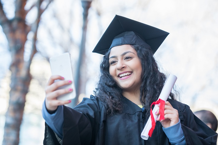 Fotka osoby v čepci a plášti pořizující si selfie z dokončení studia