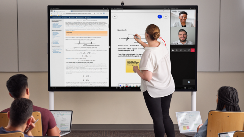 En lærer er foran en klasses håndskrift på en Hub 85" med en lyse grå Surface Pen. Edge Whiteboard og Teams er på skærmen. I forgrunden har flere studerende en Pro 7+ og tager noter i One Note.