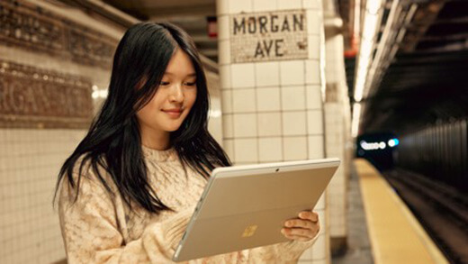 Eine Frau schaut sich ihr Surface Pro Gerät an, während sie sich in einer U-Bahnbahn befindet.