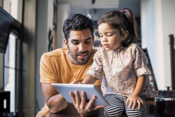 Ein Vater und eine kleine Tochter blicken auf ein Tablet