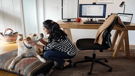 Female working remotely from her home office, taking a break and petting her dog; Dell Latitude 13 device.