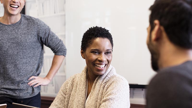 A woman and two men smiling and talking in an office