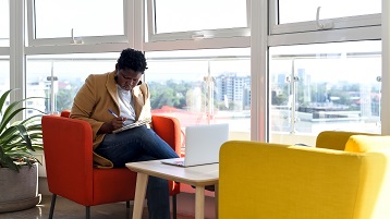 A woman takes notes in front of her computer at a remote workplace