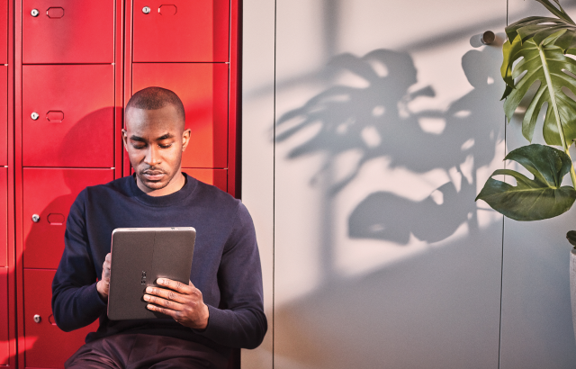 An image of a man sitting in a hallway taking digital notes on a Windows tablet
