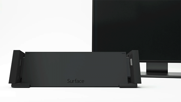 An animated graphic shows a Surface device sliding down into a docking station and a monitor behind that docking station turning on to display the same image as on the Surface
