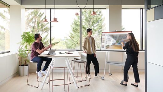 Shows a group of 3 people gathered around a Surface Hub 2S for an ad-hoc meeting.