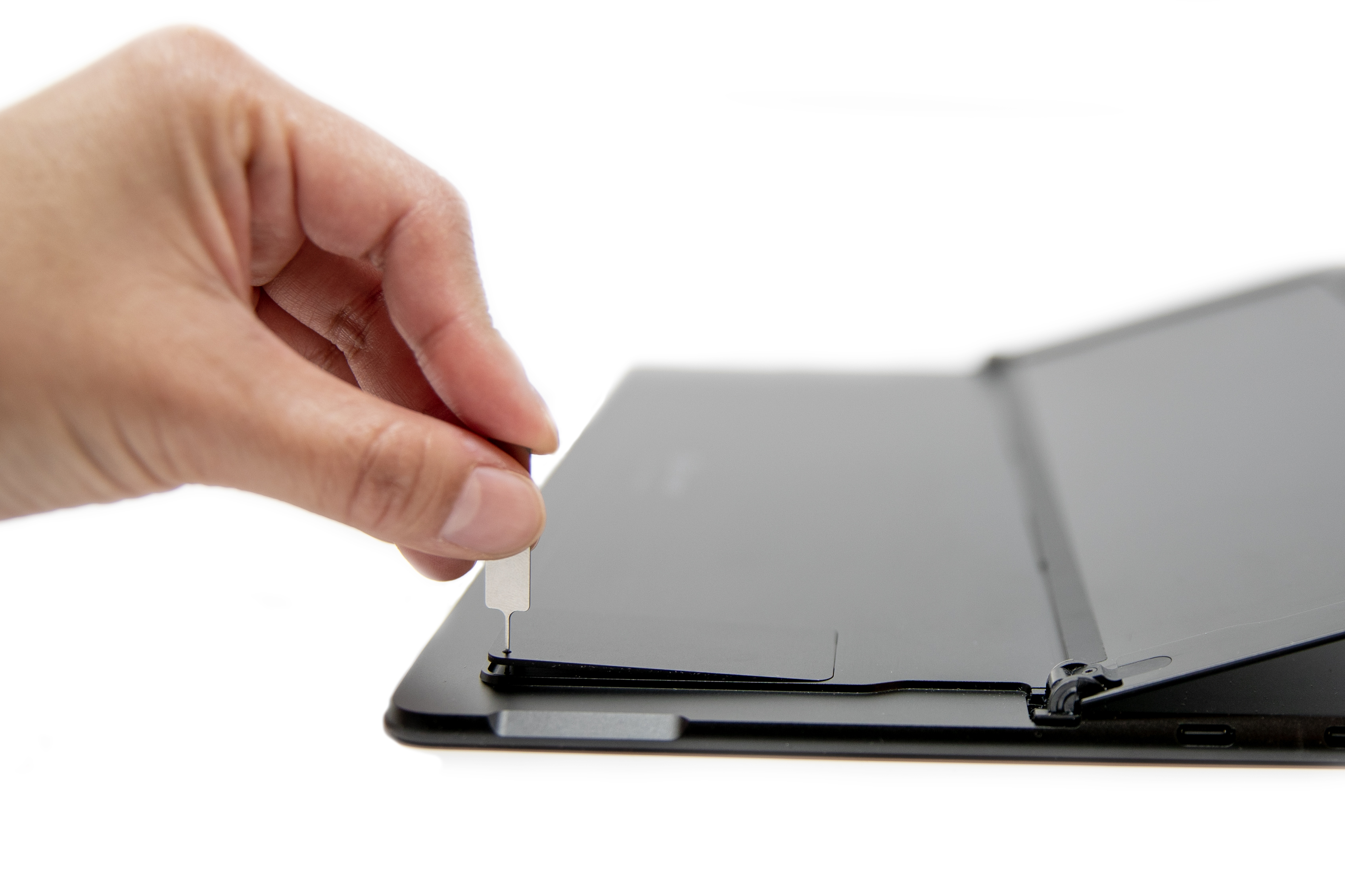 A person's hand inserted a SIM ejector into a Surface Pro X.