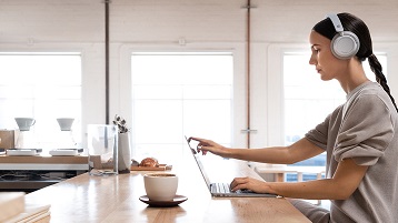 Surface Headphones -kuulokkeita käyttävä nainen työskentelemässä Surface Laptop2:n ääressä