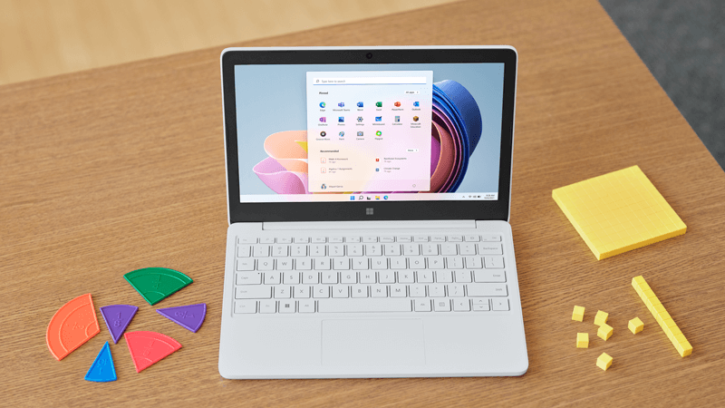 Surface Laptop SE berwarna Gletser terbuka di meja sekolah dengan layar Windows 11 SE ditampilkan.