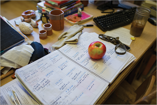 Meja pendidik dengan buku catatan, buku, apel, dan es kopi.