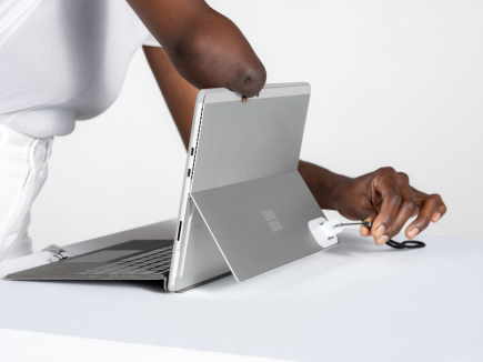 A woman uses the adaptive kit opener with a lanyard to open the Surface Pro kickstand.