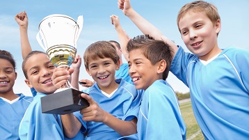 vaikų nuotrauka sporto komandoje, švenčianti pergalę ir laikanti trofėjų