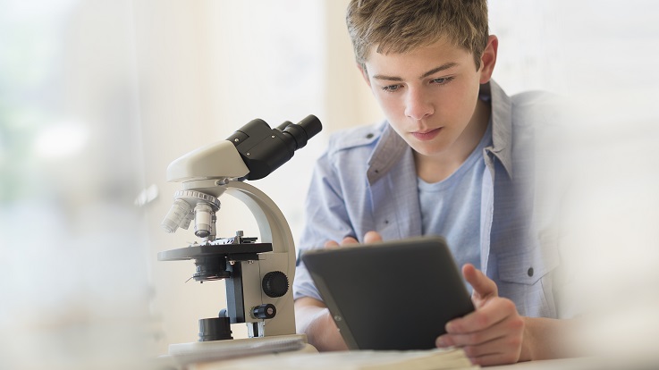 foto van een tiener die door een microscoop kijkt.