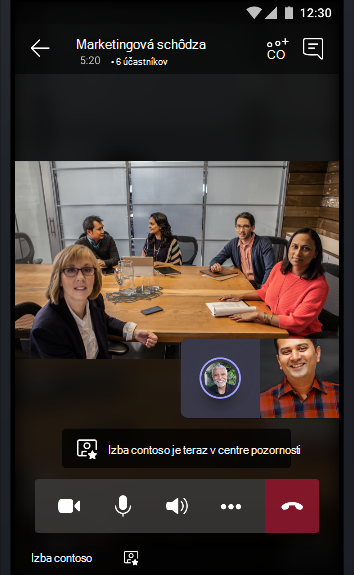 Obrázok online schôdze tímu s konferenčnou miestnosťou plnou ľudí, ktorí hovoria s ďalšími dvomi účastníkmi schôdze.