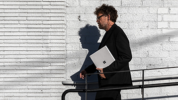 Moški med hojo in v roki drži Surface Book