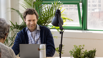 Зображено молодого чоловіка з ноутбуком на сучасному робочому місці в невеликій організації.